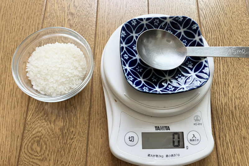 小皿に入れた生米とキッチンスケール、大さじを並べて計量準備をしている様子